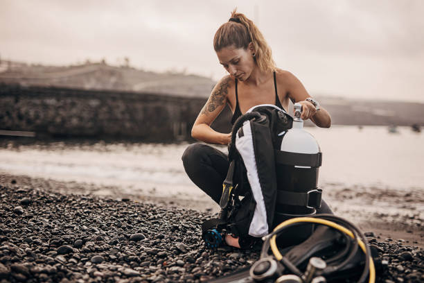 ウェットスーツの女性ダイバーが水に入る前に酸素タンクを準備する - oxygen tank underwater diving diving wetsuit ストックフォトと画像