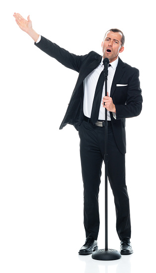 Front view of aged 40-44 years old with brown hair caucasian male singer dancing in front of white background wearing businesswear who is singing and holding microphone stand