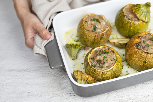 Stuffed round courgettes meal cooking preparation - hand is holding hot baking dish with freshly baked vegetables