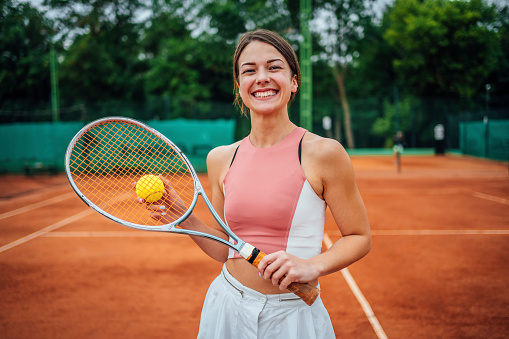 Active smiling young woman on the tennis court with tennis racket in hand