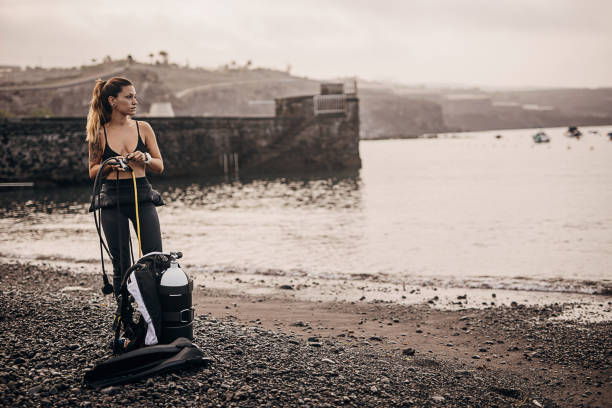 ウェットスーツの女性ダイバーが水に入る前に酸素タンクを準備する - oxygen tank underwater diving diving wetsuit ストックフォトと画像