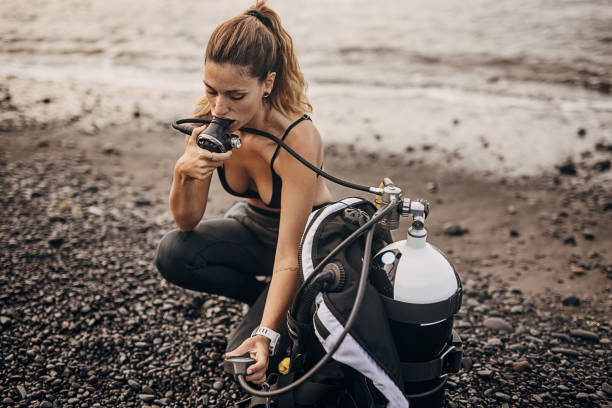 ウェットスーツの女性ダイバーが水に入る前に酸素タンクを準備する - oxygen tank underwater diving diving wetsuit ストックフォトと画像