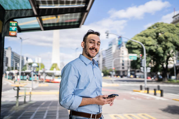retrato de um jovem usando o celular no ponto de ônibus - satisfaction clothing argentina smiling - fotografias e filmes do acervo