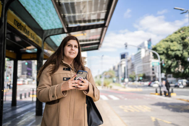 istock Young woman using the mobile phone at the bus stop 1401528535