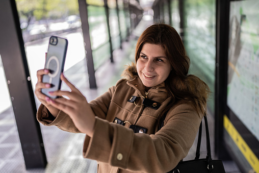 Young woman taking selfies on the mobile phone at the bus stop