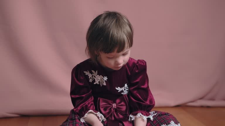 Cute little girl in an vintage burgundy dress is playing with a hair clip