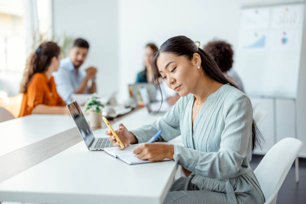 The star of the company Asian businesswoman working at her desk in a bright modern office with colleagues in the background central asian ethnicity stock pictures, royalty-free photos & images