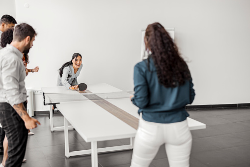 Group of happy businesspeople playing ping pong table tennis at office.