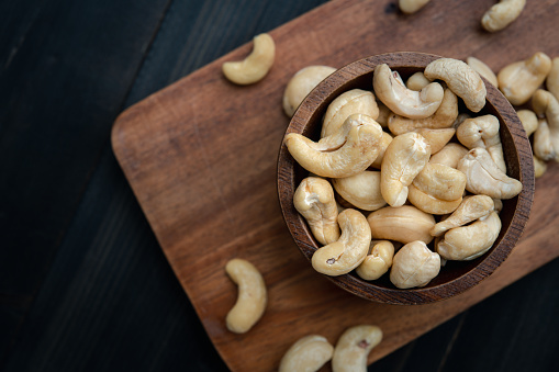 raw cashew nuts in wooden bowl on rustic table, healthy vegetarian snack