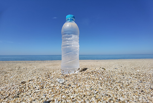 water bottle frozen cold on the sand of the beach in a hot summer day  blue sea and sky bacikground