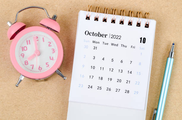 istock October 2022 Desk calendar with pink alarm clock on brown background. 1401539542