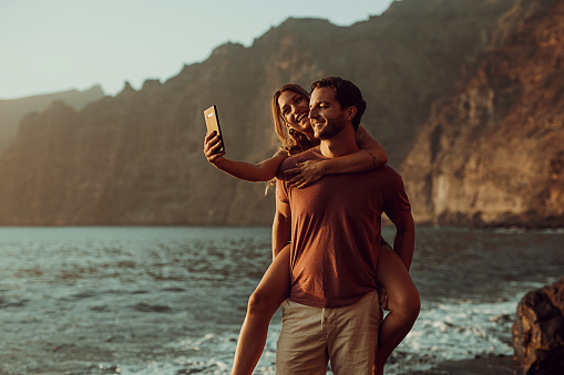 Couple is having fun and taking a selfie on the beach at sunset