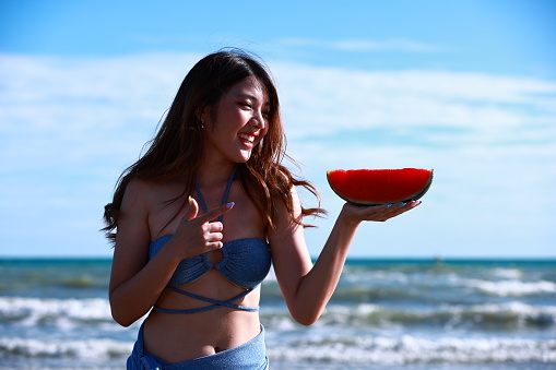 Joyful young woman wearing swimming dress with watermelon slice on tropical beach