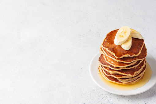 Stack of banana pancakes with syrup on a white plate, gray background, copy space. Vegan recipe concept.