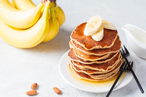 Stack of banana pancakes with syrup on a white plate, gray background. Vegan recipe concept.