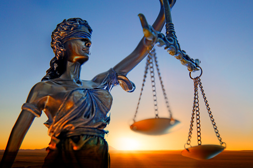 A statue of lady justice stands in front of a setting sun.