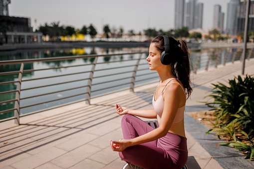 Woman meditating and listening music in public park