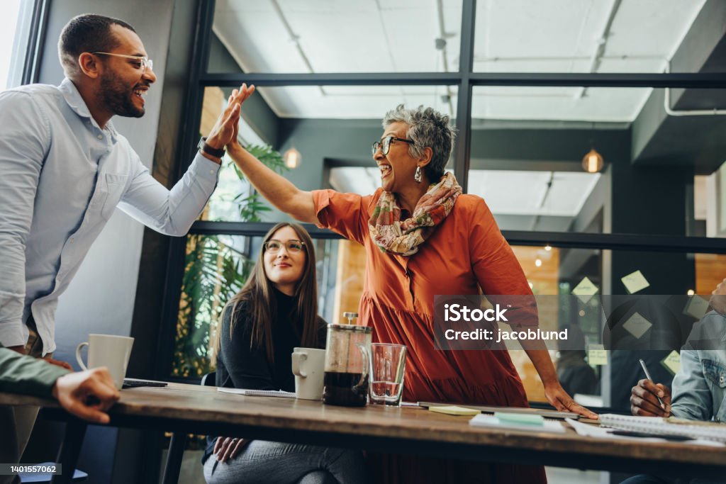 Cheerful business colleagues celebrating their success Cheerful business colleagues high fiving each other during an office meeting. Successful businesspeople celebrating their achievement. Happy businesspeople working as a team in a creative workplace. High-Five Stock Photo
