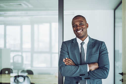 Portrait of confident african-american businessman standing in his office with crossed arms and looking at camera.