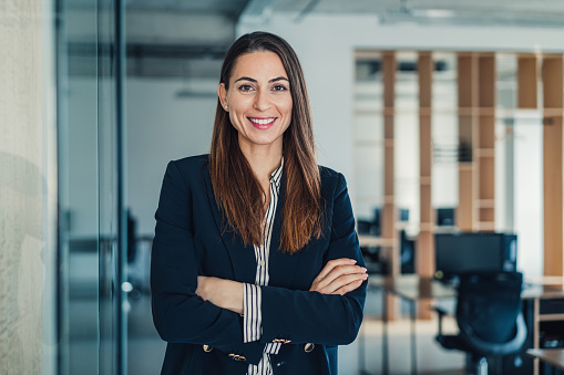 Happy smiling confident middle aged Asian older senior female leader businesswoman standing in modern office workplace looking at camera arms crossed. Business successful executive concept. Portrait.