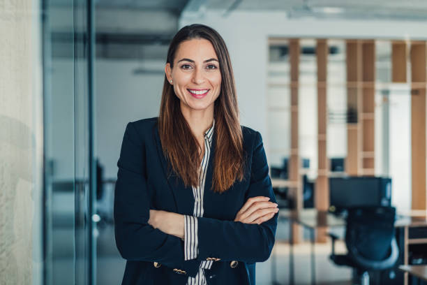 Confident businesswoman in modern office. Shot of beautiful smiling businesswoman standing with crossed arms in her office and looking at camera. professional woman stock pictures, royalty-free photos & images