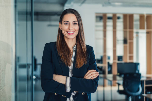 Confident businesswoman in modern office. Shot of beautiful smiling businesswoman standing with crossed arms in her office and looking at camera. businesswoman stock pictures, royalty-free photos & images
