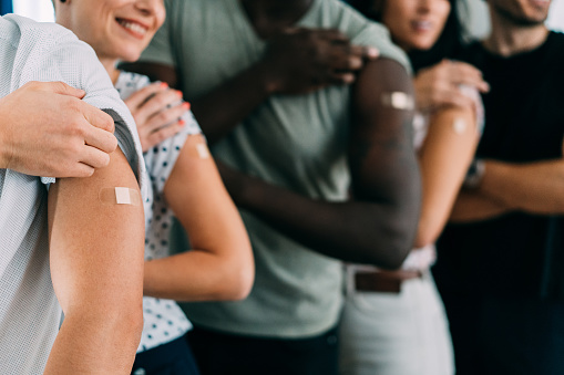Group of friends showing their arms with a bandage after receiving COVID-19 vaccine. Young business people showing their shoulders after getting coronavirus vaccine.