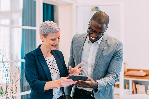 Shot of two successful businesspeople working together on a tablet in modern office. Businessman and businesswoman in meeting using digital tablet and discussing business strategy. Two business people talking in the office.