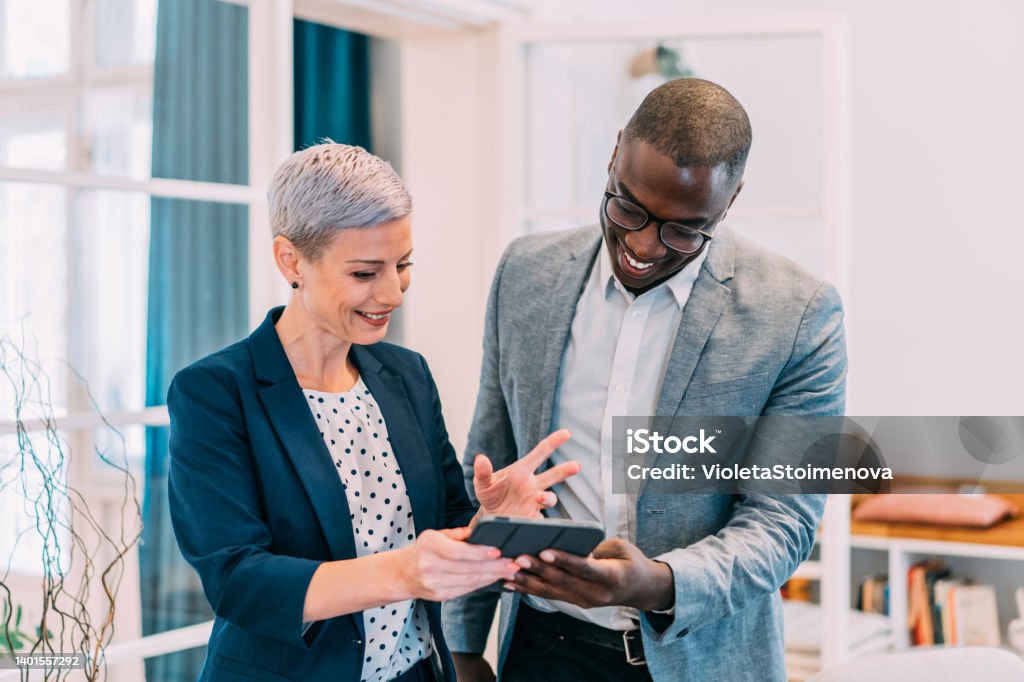 Confident business partners working on digital tablet in office. Shot of two successful businesspeople working together on a tablet in modern office. Businessman and businesswoman in meeting using digital tablet and discussing business strategy. Two business people talking in the office. Digital Tablet Stock Photo
