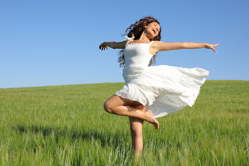 Happy woman twirling with white dress in a field