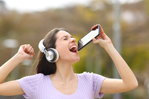Happy teen singing in the street using phone as mic
