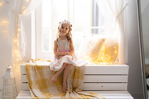 Portrait of a little girl wearing dress sitting on a wooden white window at home