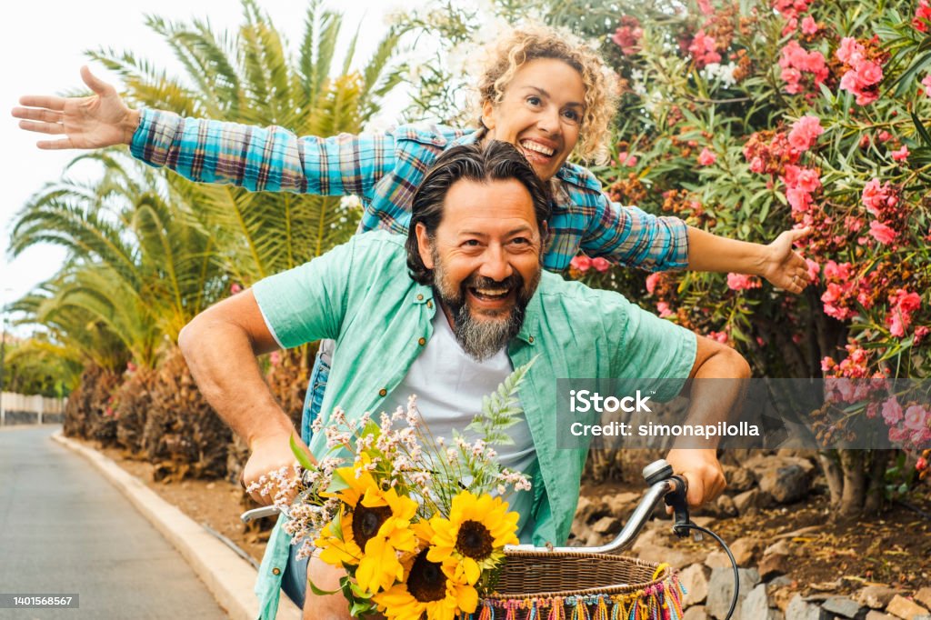Happy people couple having fun riding a bike together. Man carrying woman on the road. SPring nature in background. Outdoor leisure activity for two male and female enjoying active lifestyle Cycling Stock Photo