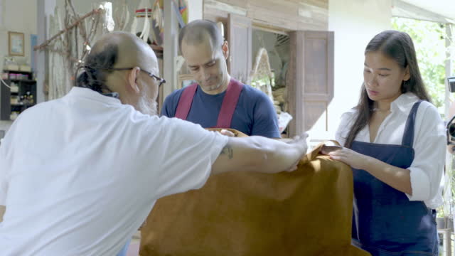 A man teaches a couple how to make leather goods.