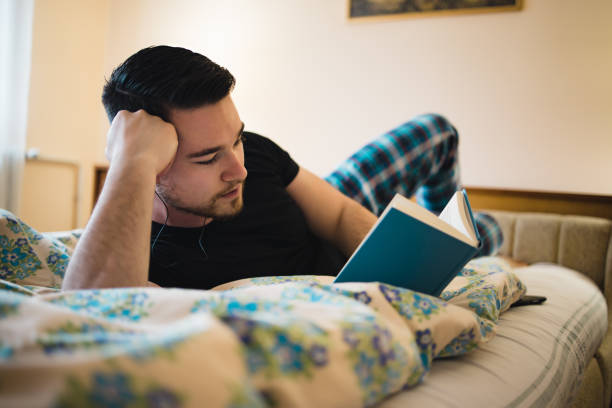 istock Young handsome man laying on bed,resting and reading a book. 1401572562