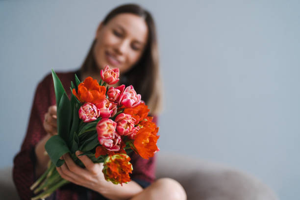 Happy woman enjoy bouquet of tulips. Housewife enjoying a bunch of flowers and interior of kitchen. Sweet home. Allergy free