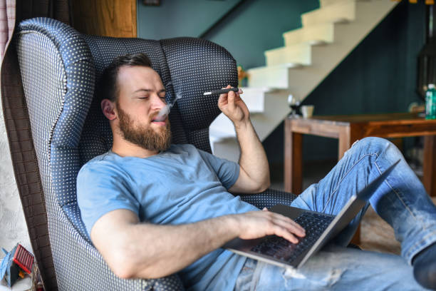Smoking Male Working From Home And Getting Lucrative Business Done Smoking Male Working From Home And Getting Lucrative Business Done vape pen stock pictures, royalty-free photos & images