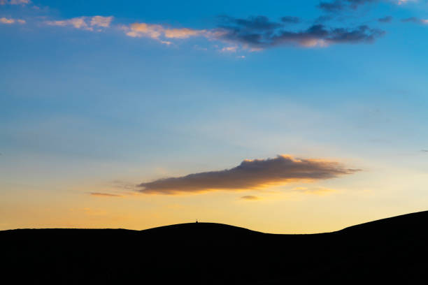 Sunset is reflected golden light by the river on grassland with mountain in background.