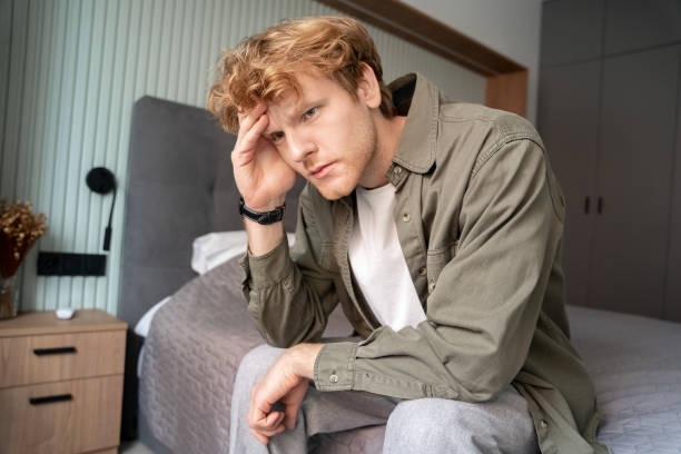 istock Young ginger man holding painful head sitting on bed selective focus 1401578827