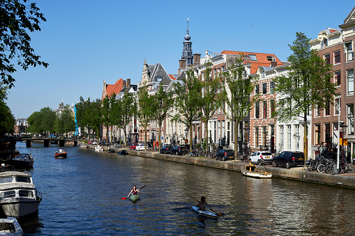 City canal with two people kayaking on a summer day with clear blue sky, Amsterdam, The Netherlands.