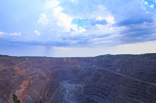 Open pit iron ore mining. Drill rigs and excavators in the process . Heavy steel industry initial production chain . Thunderstorm clouds over the quarry.