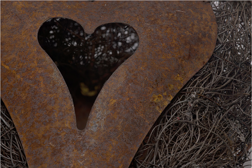 Extreme close up of three dimensional rustic vintage retro heart made of rusty iron against woven background of branches