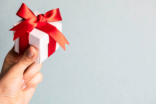 Woman's hand holding gift box in front of blue background.