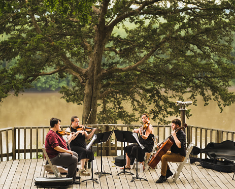 View of chamber quartet of two young men and two young women musicians playing concert on wooden deck above Missouri River on summer evening