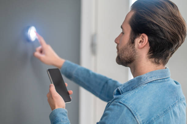 istock Man with smartphone touching button on wall indoors 1401587407