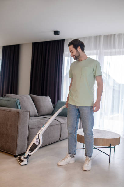 istock Cheerful man vacuuming floor in room 1401587451