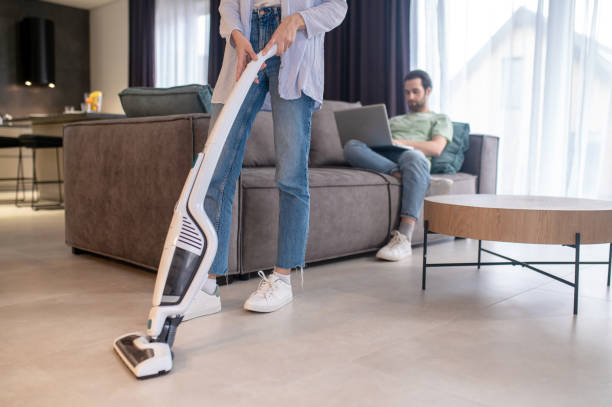 istock Man looking at laptop woman vacuuming floor 1401587454