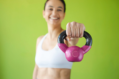 Woman is in gym clothes working out with a kettlebell against a yellow background.
