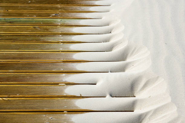 Wind created pattern of light fine beach sand on brown outdoor patio boards