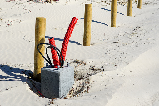 Concrete base of a new lighting lantern pole with screws and supply cable outlets on a sandy beach